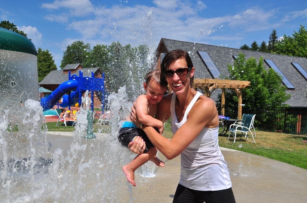 A father holds his baby while enjoying a splashpad at Photo Courtesy: The Tyler Place Family Resort, one of the best Vermont hotels for families.