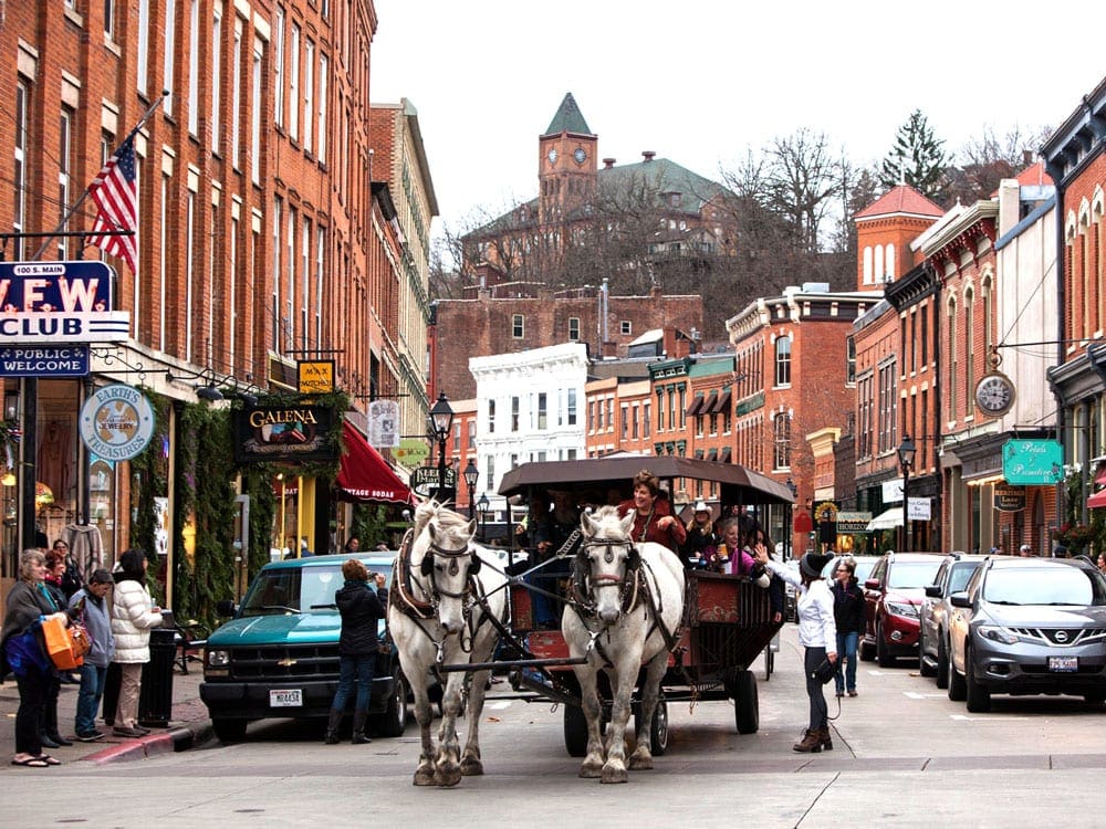 A buggie is pulled by two white horses down the main street of historic Galena, IL, one of the most charming towns to visit with kids.