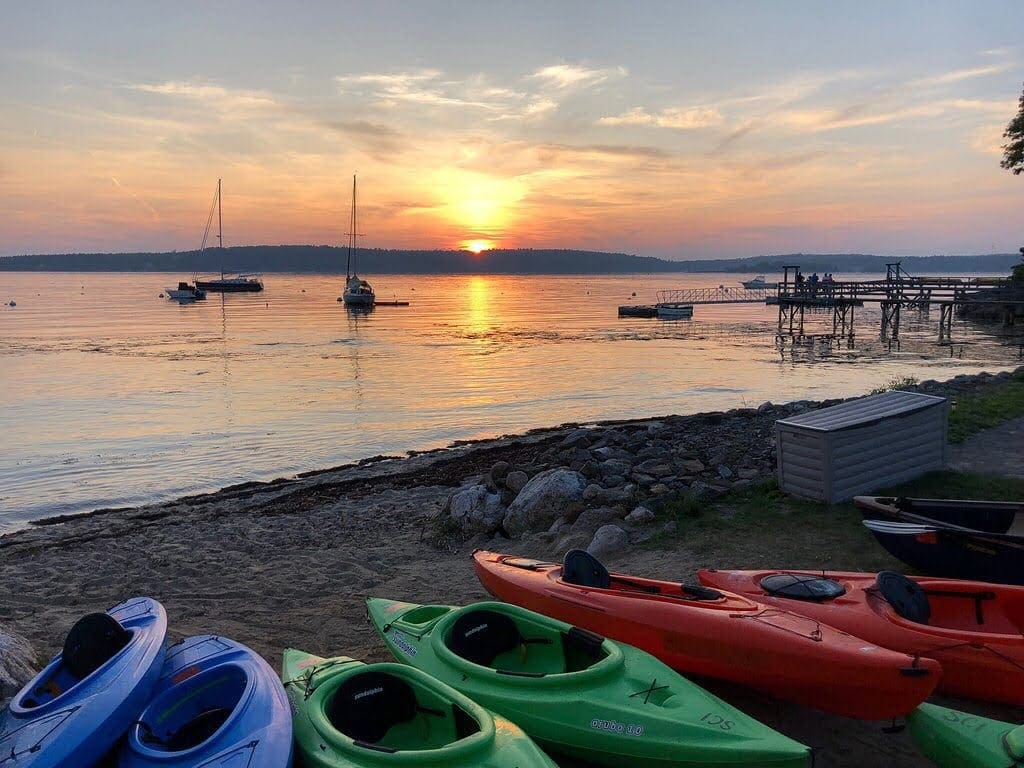 Several colorful kayaks rest quietly on the beach during a Maine sunset at Smuggler's Cove Inn, one of the best Maine hotels for families.