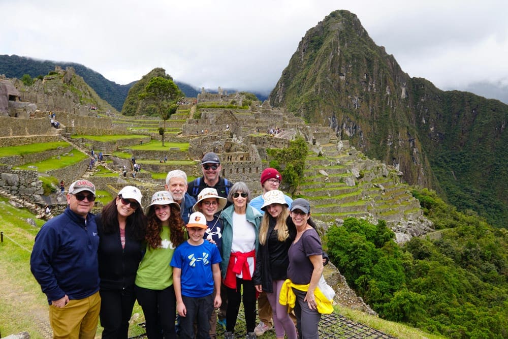 A large multigenerational family stands in front of Machu Picchu, one of the vacations to plan a year in advance.