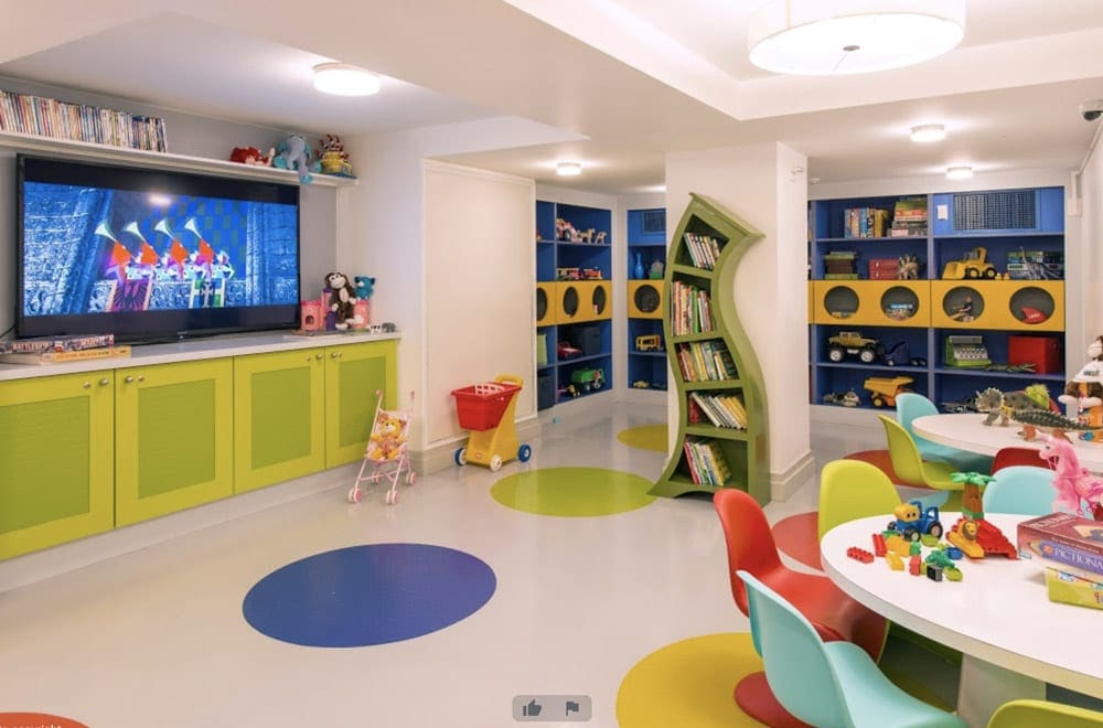Inside the colorful kids club at Boca Beach Club, A Waldorf Astoria Resort, featuring a large TV, toys, and a table with chairs.