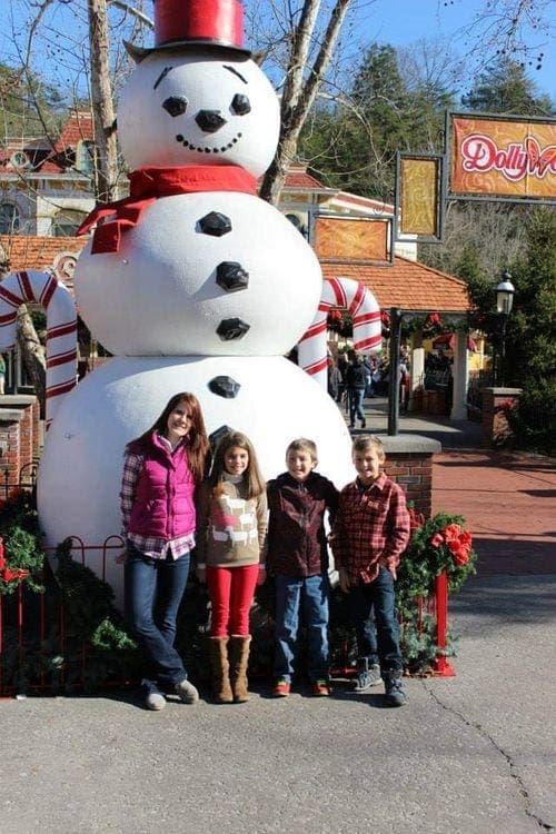 A mom and her three children stand in front of an enormous snowman display in Gatlinburg, one of the most magical Christmas towns for families.