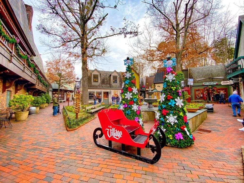A large red sleigh sits on a brick street surrounded by Christmas tress in Gatlinburg, Tennessee, one of the most magical Christmas towns for families.