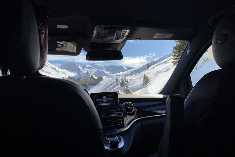 A man sits in the driver's seat of the car looking out at a wintery landscape in St. Moritz.