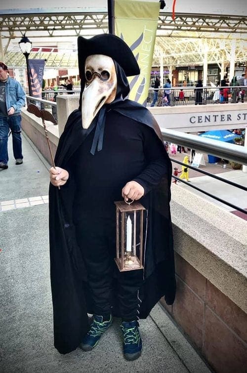 A pre-teen boy wears a plague doctor's mask and holds a candle as part of a travel inspired Halloween costume.