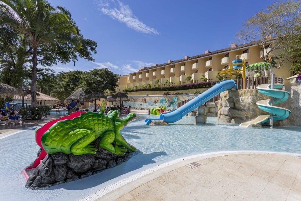 A splash pad featuring a large alligator and slides, while Grand Palladium Vallarta Resort & Spa stands in the background.