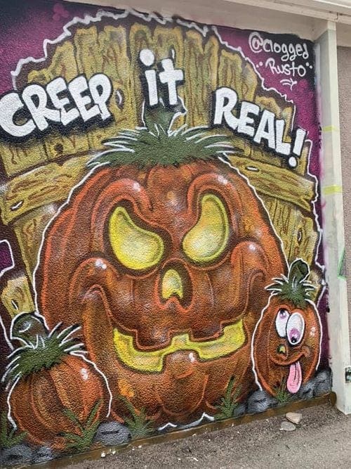 Street art in Kansas, City, Misuri featuring a large orange pumpkin sitting in front of a fence with the text "Creep It Real!".
