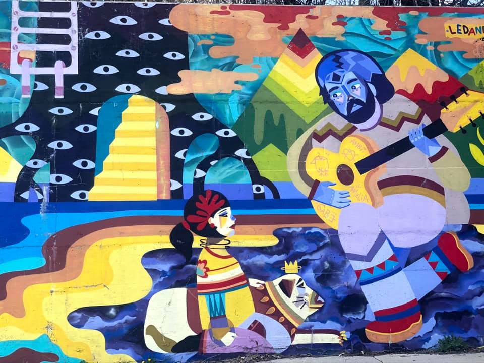 A street art mural in Detroit, featuring indigenous symbolism, as well as a man playing a guitar.