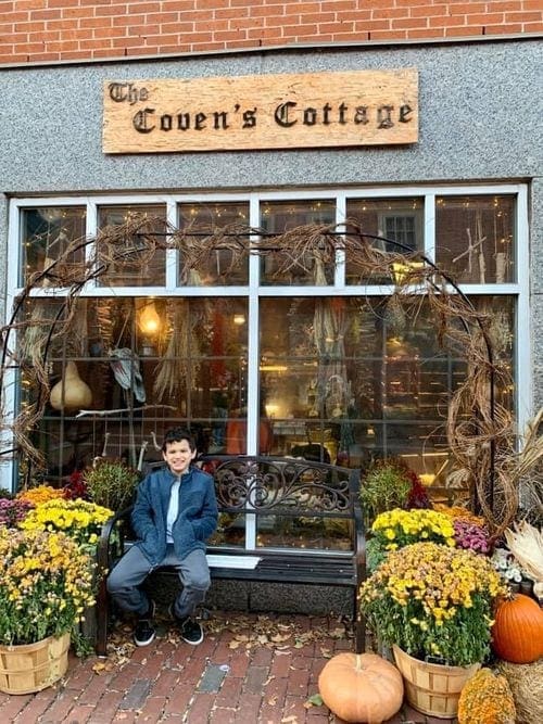 A young boy sits in front of a storefront in Salem, Massachusetts, decorated for the Halloween season.