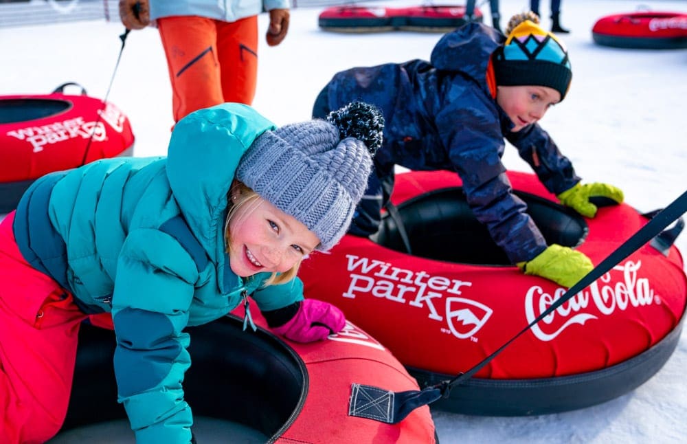 Two kids lay in large red snow tubes at Winter Park, offering some of the best Colorado snow tubing for families.