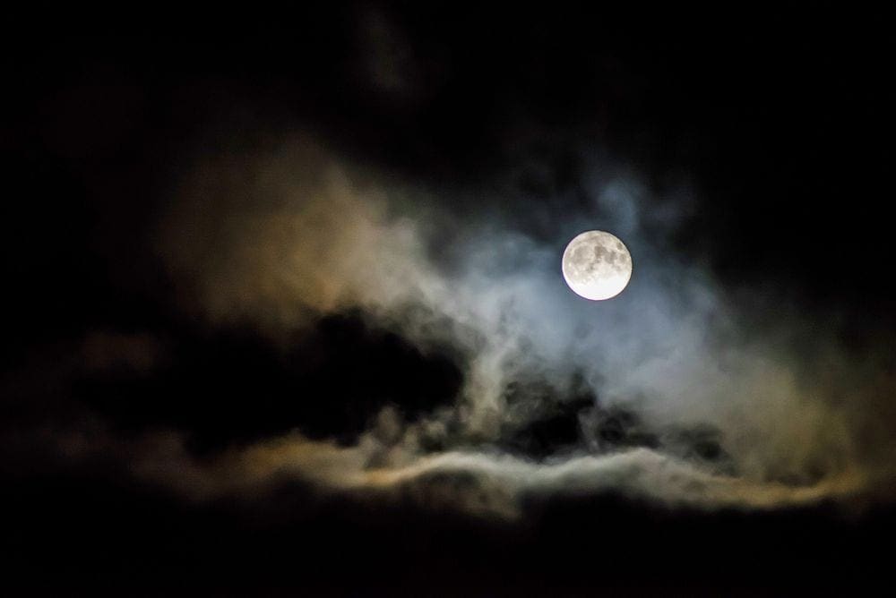 The moon is tucked behind a series of clouds, giving it a spook ambiance.