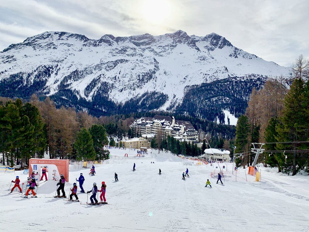 Suvretta House Ski School at St. Moritz, featuring a snowy mountain and several skiers in the distance. Finding a kid-friendly resort is one of the best tips for skiing with kids for the first time. 