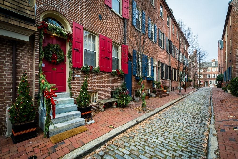 A cobblestone street in Philadelphia, with several houses outfitted in garland and wreaths for Christmas.