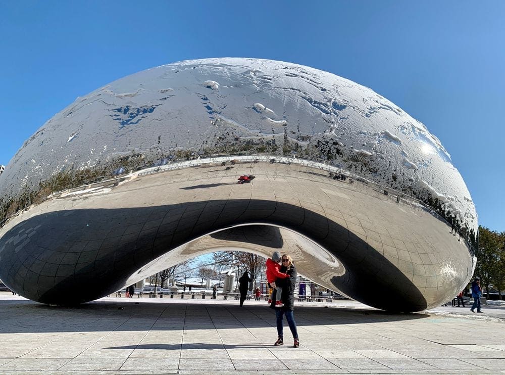 A mom holds her son in front of a snow-covered Bean in Chicago, Illinois.