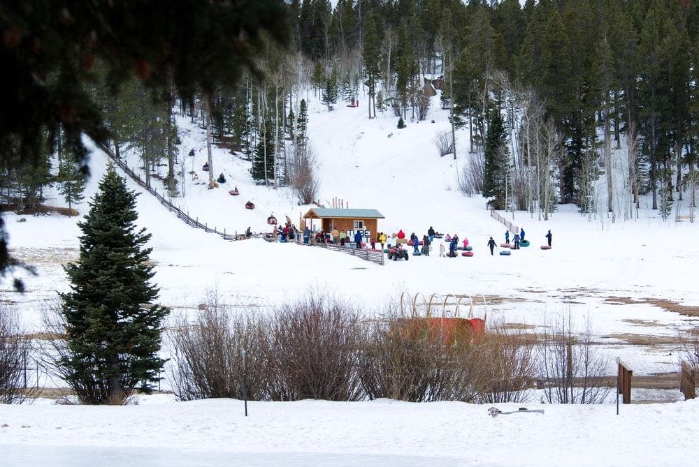 A number of people holding or sitting on snow tubes are seen in the distance at Beaver Meadows Resort Ranch, one of the best Colorado snow tubing spots!