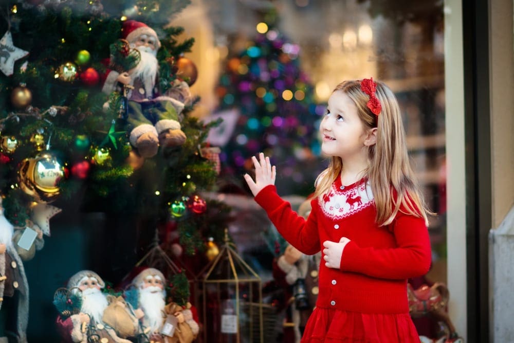 A young girl wearing a red dress looks up at a lovely Christmas tree.