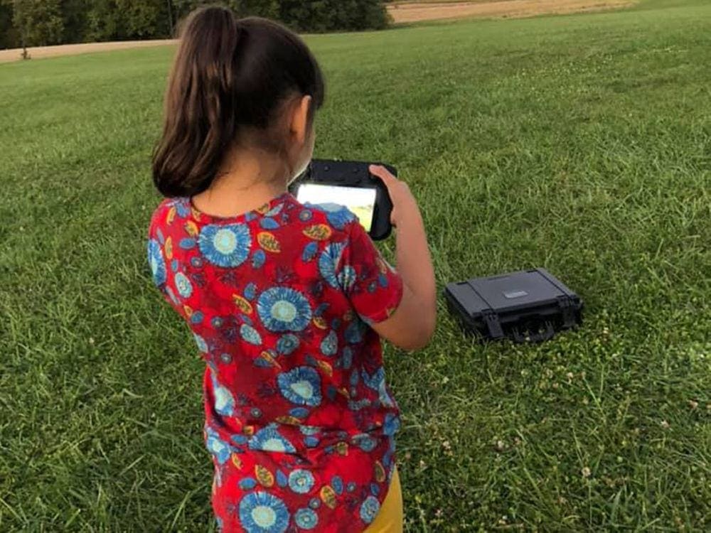 A young girl looks at the screen of her drone, one of the best outdoor gifts for families, in a grassy field.