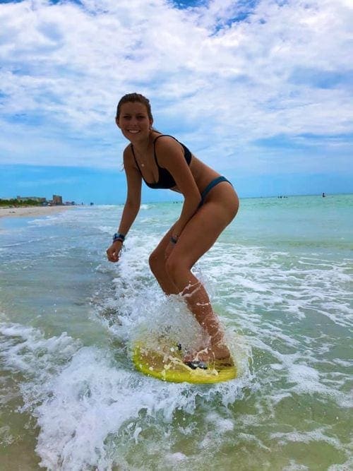 A woman balances on a boogie board along a wave.