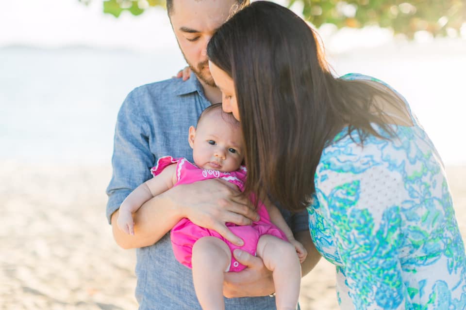 A mom and dad hold and kiss their infant daughter while on the beach at St. Thomas.