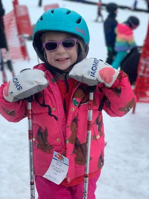 A young girl, wearing a pink ski suit, leans on ski poles at Ski Butternut.