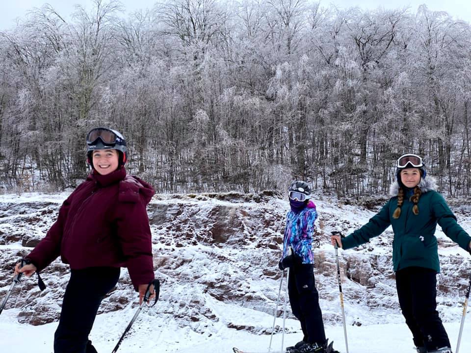 Three teenagers stand on skis while smiling at Belleayre Mountain.