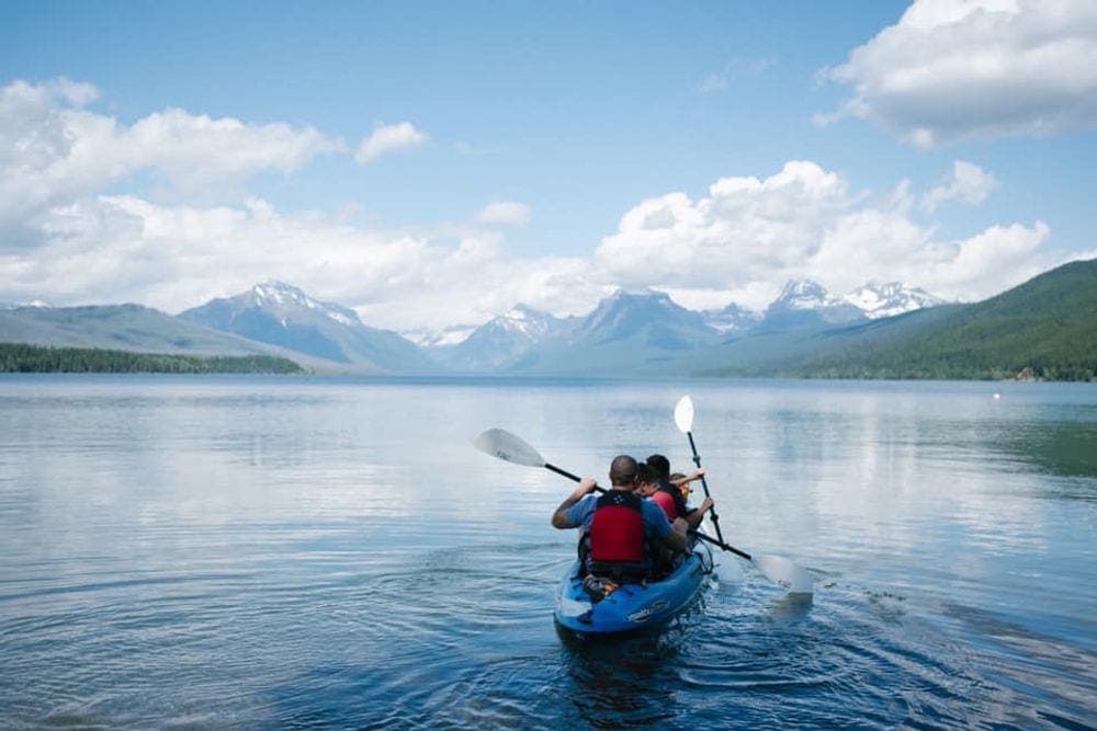 Kayakers embark on a lake journey, with mountains in the background.