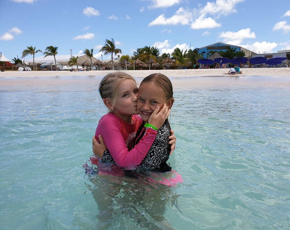 A young girl gives her sister a kiss in the water, off the beach in the Bahamas, one of the best Caribbean islands for families.