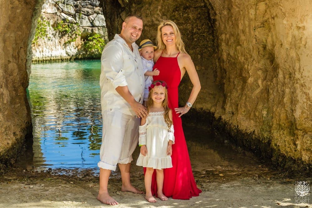 A family of four stands smiling in front of a on-site lagood at Hotel Xcaret.