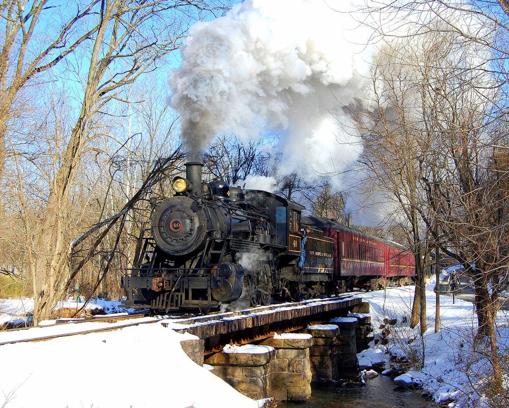A large steam engine barrels down a wooded railroad, covered in snow.
