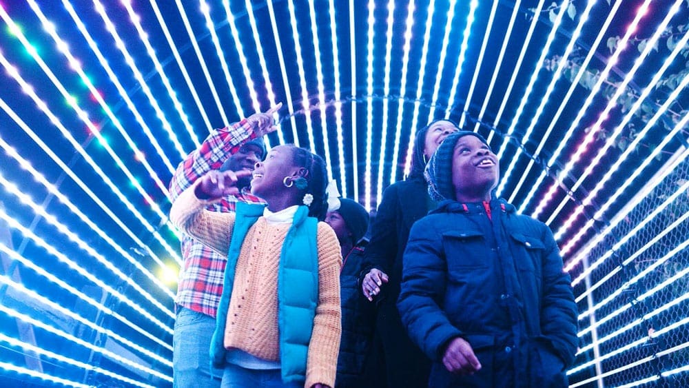 A family of color admires a lighted tunnel, as part of the holiday display at Elmwood Park Zoo, one of the best things to do in Philadelphia with kids this winter.