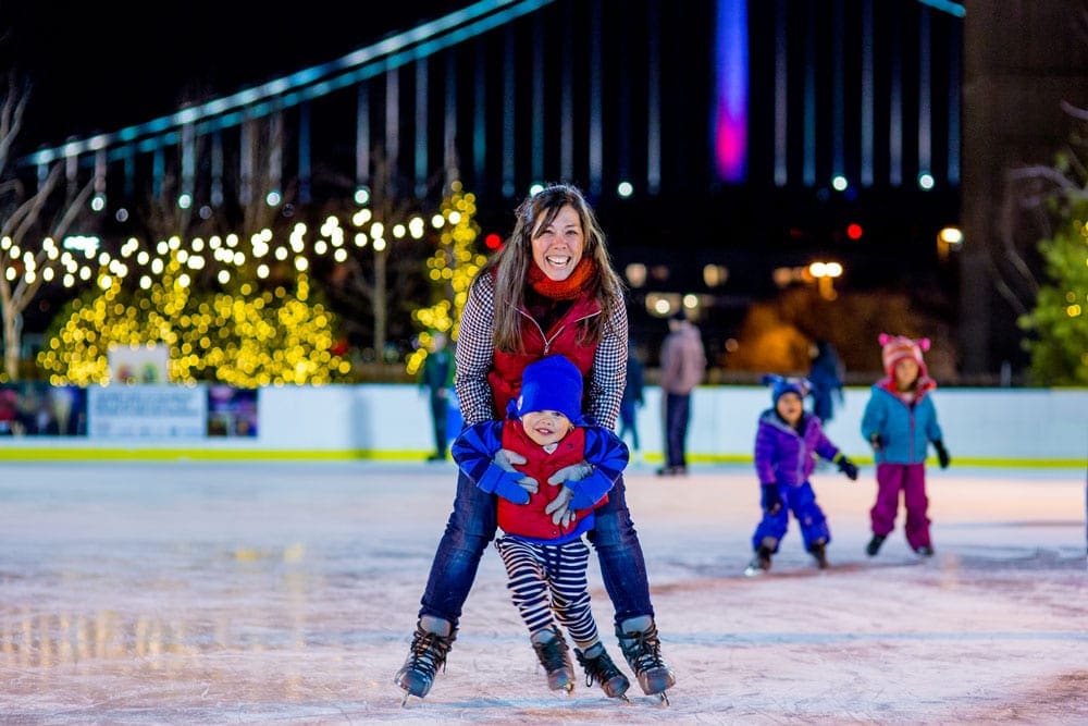A mom hugs her son from behind him while they skate on the ice at River Rink, one of the best things to do in Philadelphia with kids this winter.