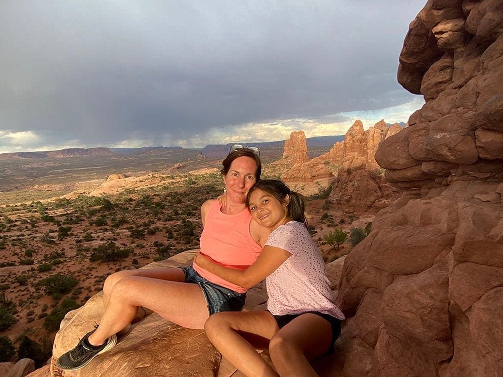 A young girl hugs her mom as they sit amoung the rocks at Arches National Park.