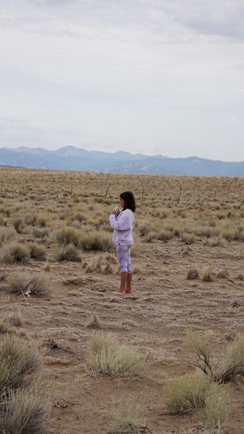 A young girl stands among sand dunes on a clear day.