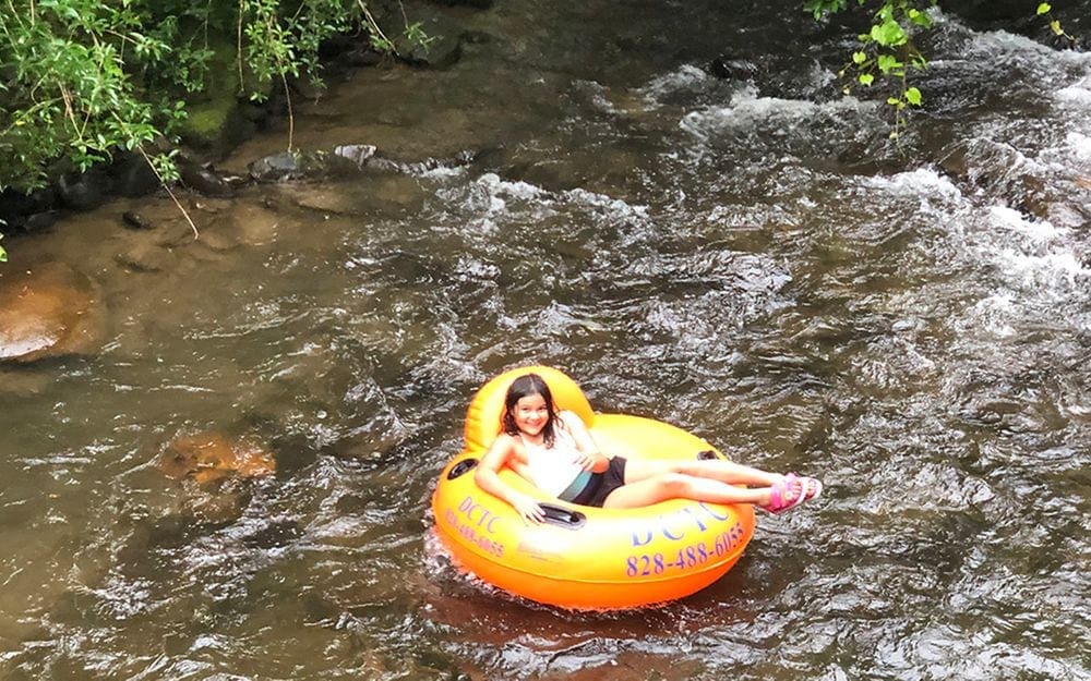 A young girl sits in a tub floating down a river within the Smoky Mountains National Park.