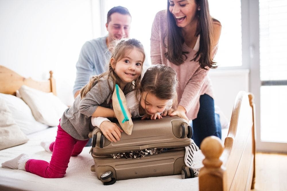 A family of four sits on a bed packing a suitcase awaiting a trip signing up for the Southwest companion pass promotion.