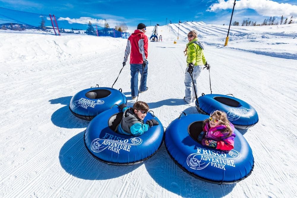 Two parents pull their snow tubes, as well as snow tubes with their two kids inside, in the snow at Frisco Adventure Park, one of the best Colorado snow tubing spots!