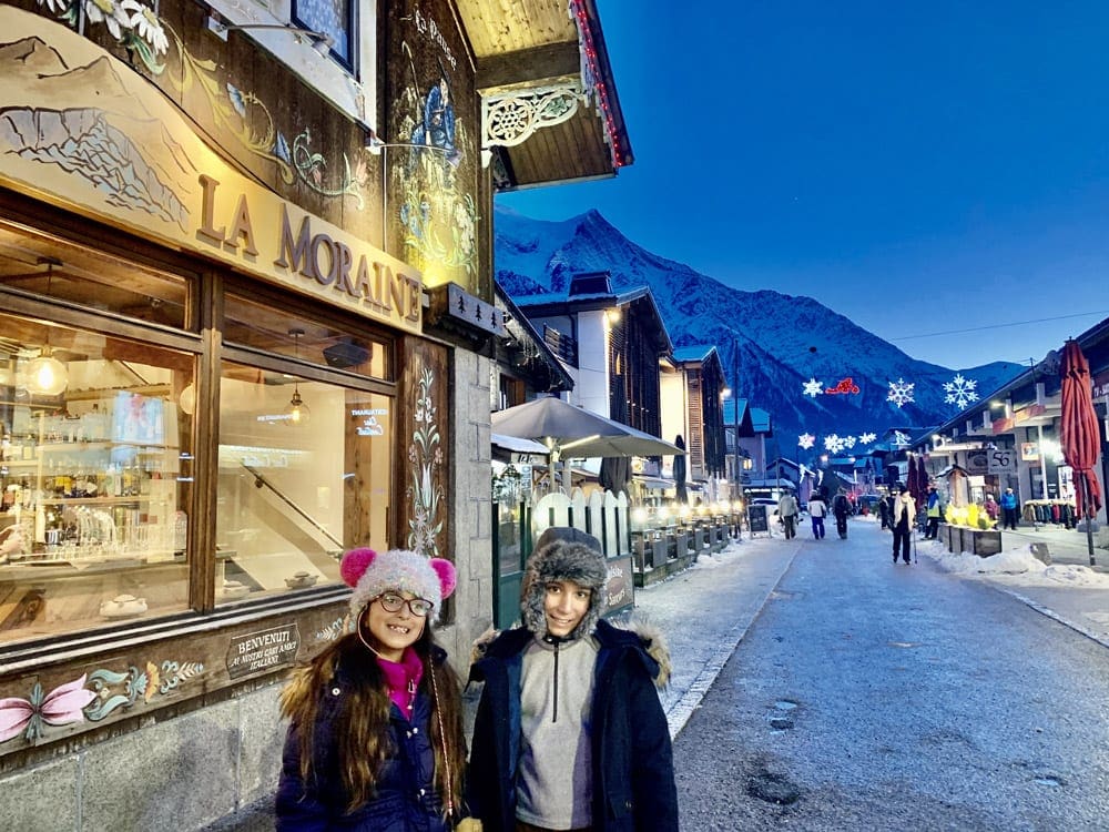 Two kids stand outside of a bakery on a snowy winter's night in Charmonix.