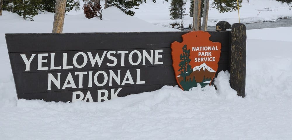 The sign for Yellowstone National Park covered in snow.