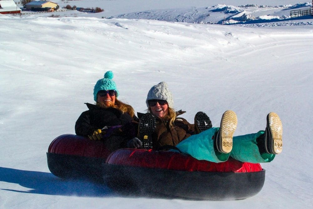 Two women ride tandem in a snow tube down a hill at Steamboat, one of the best Colorado snow tubing spots!