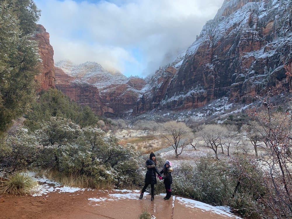 Mom and daughter holding hands and slowly Zion National Park in the background 