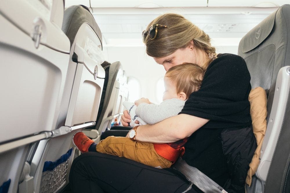 A mom holds her infant son on an airplane.