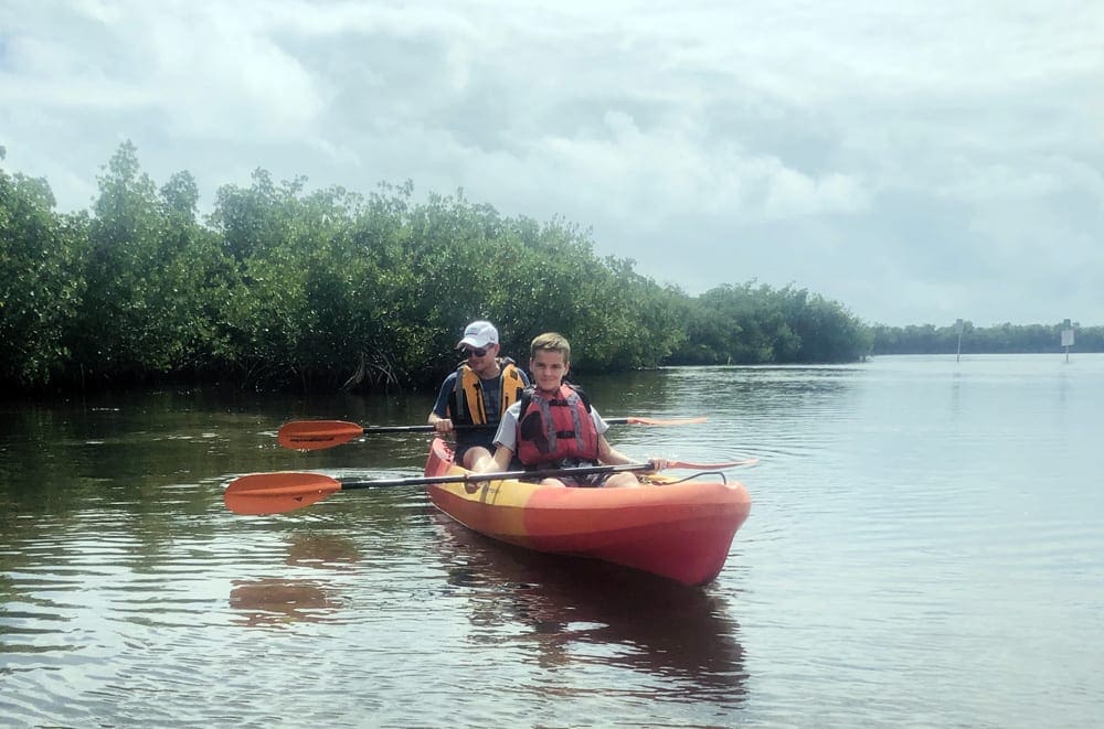 Father and son paddling on a kayak with greenery in the background.  