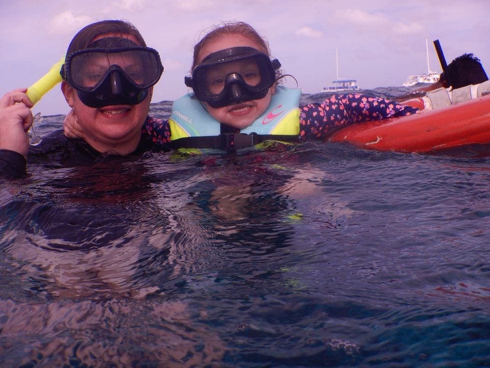 A mom holds onto her young daughter, who holds onto a red floatation device, while snorkeling in Cozumel.