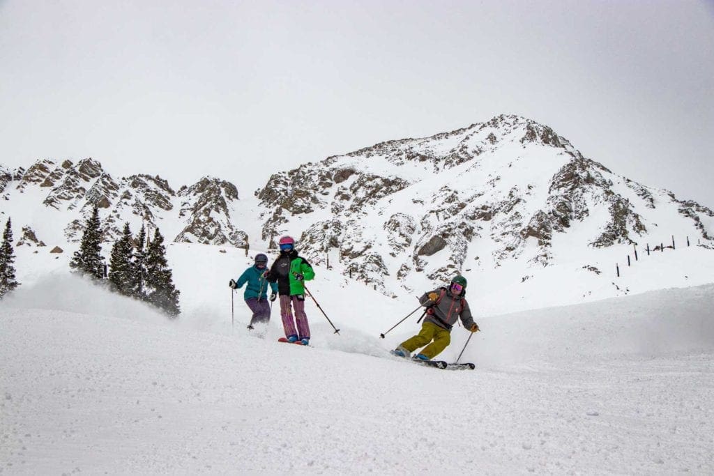 Three skiers wind through the powder at Arapahoe Basin, best small ski resorts in Colorado for families.