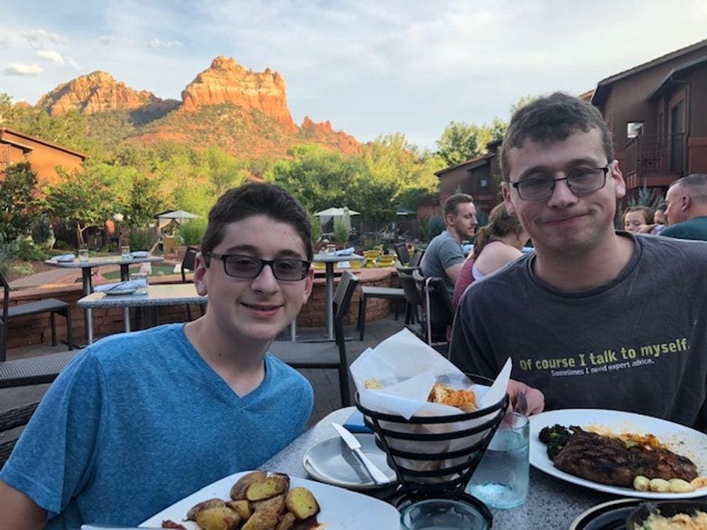 A dad and son smile before eating their meal at the Amara Hotel in Sedona with the red rocks in the background.