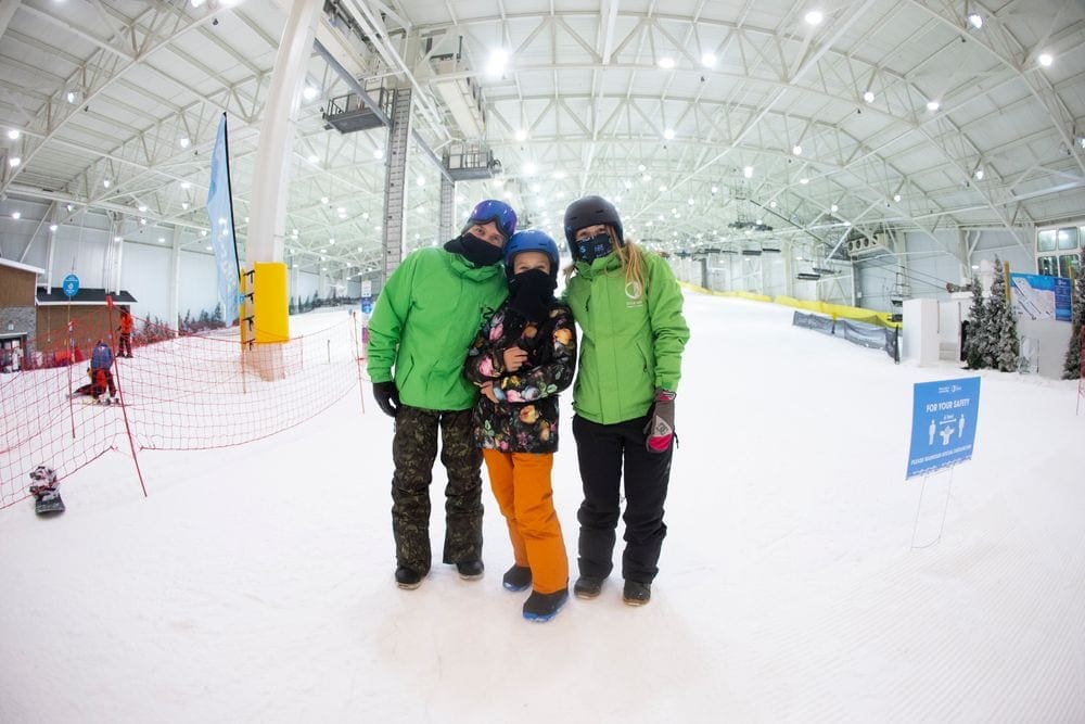 A family of three in full snow gear, helmets, and masks, stand inside Big SNOW American Dream.