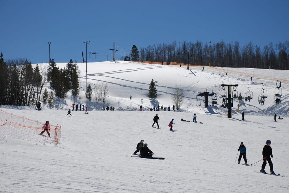 A view of the slopes at Granby Ranch, best small ski resorts in Colorado for families, featuring dozens of skiers and a chair lift.