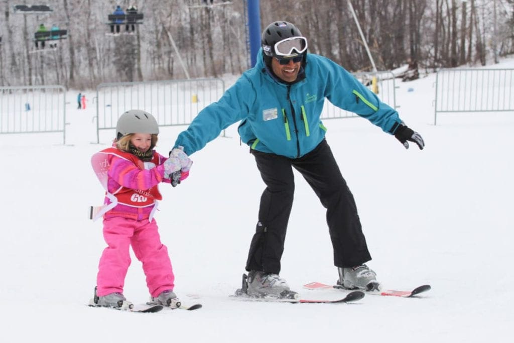 A young girl on skis holds onto the hand of her ski instructor at Liberty Mountain Resort, one of the best options for skiing near DC with kids.