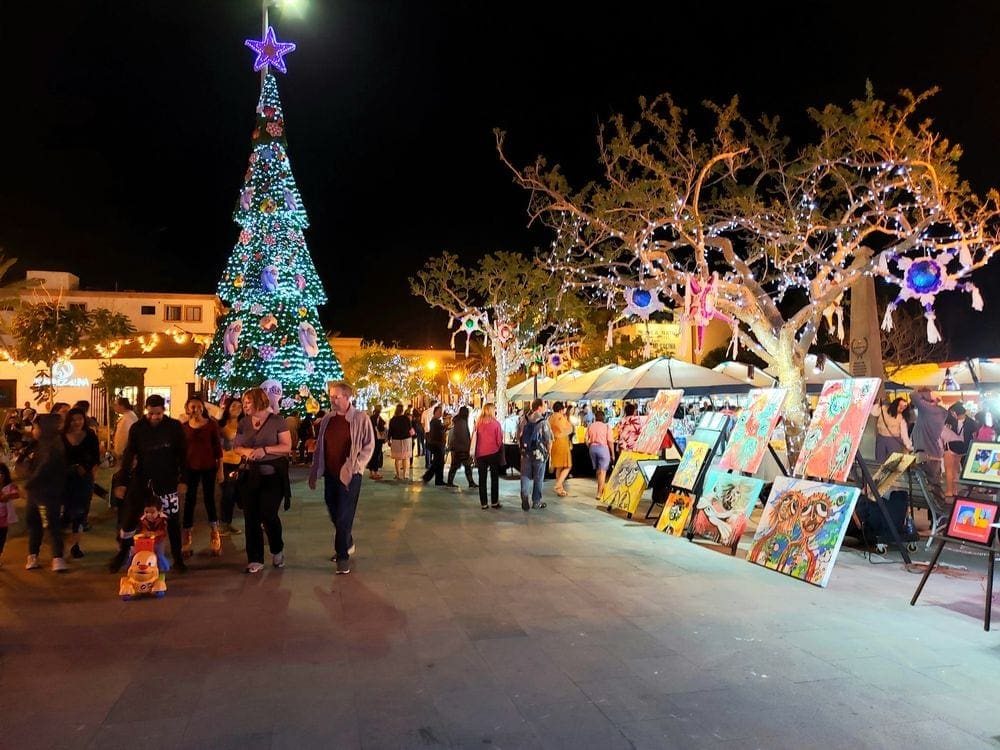 The art walk in Los Cabos, where several people are walking around looking at art and the holiday lights in the background.