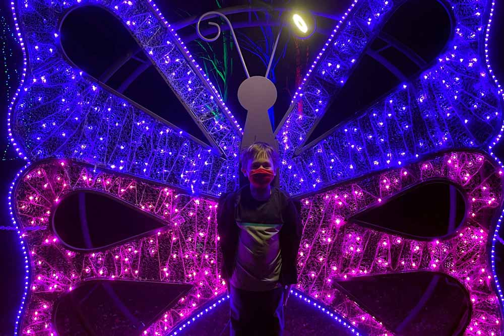 A young boy stands in front of a holiday light display, making it look like he has butterfly wings.